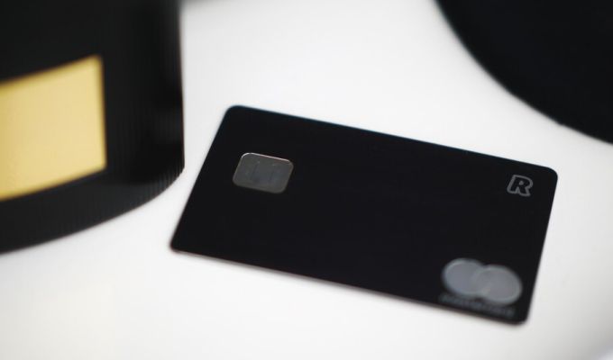 Czarna, minimalistyczna karta płatnicza z widocznym chipem i logo Mastercard leżąca na jasnym tle.