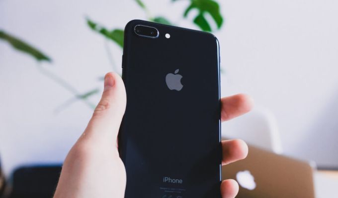 Osoba trzyma w ręku czarny smartfon z logo firmy Apple.
