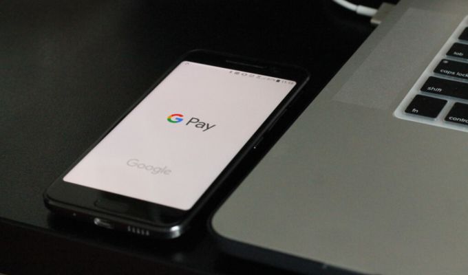 Smartfon leży na biurku obok laptopa. Na ekranie telefonu widać napis GPay.